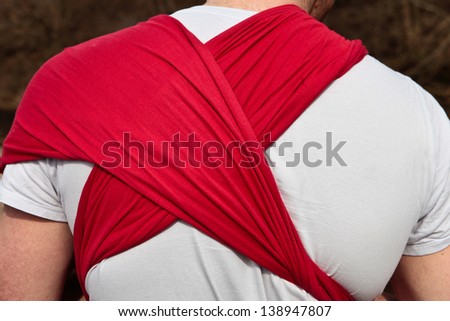Red cloth baby sling on the back of a young father
