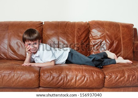 A six year old boy reclining on a leather sofa