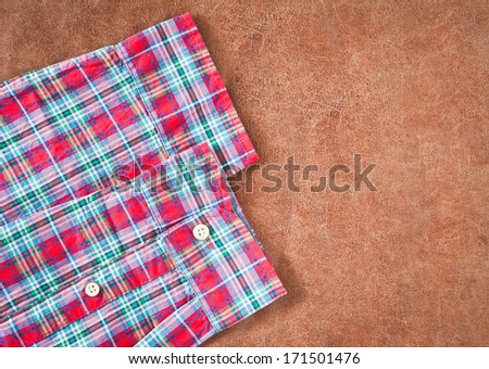 Red tartan patterned shirt sleeves on a leather background