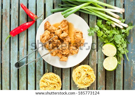 Freshly cooked chicken pieces on a small plate with raw ingredients and dried noodles