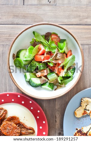 Fresh garden salad and plates of starters on a wooden table