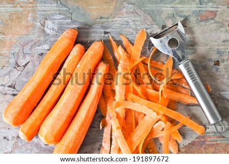 Raw carrots on a worktop with a peeler