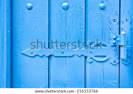 Decorative hinge on a blue painted wooden door with rain drops