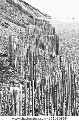 A wooden fence at the base of a cliff in the UK to protect against falling rocks, in black and white