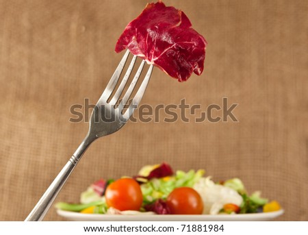 Nice image of a fork holding a leaf of red lettuce with a plate of mixed salad in the background