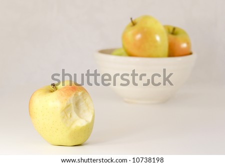 an apple missing a bite in front of a bowl of apples