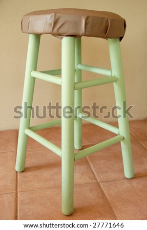 a simple wooden stool with vinyl upholstered seat on ceramic tile floor