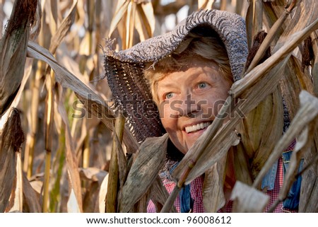 an aging woman wearing a straw hat standing among corn stalks