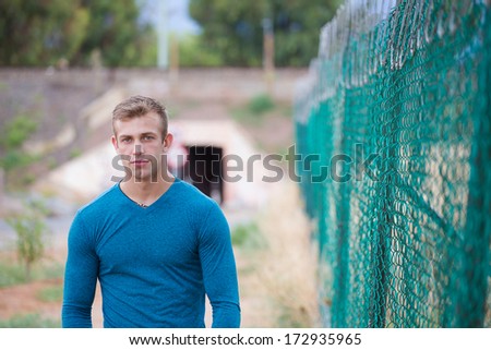 A Good looking male model walking past a fence, wearing trousers and a long sleeved t-shirt