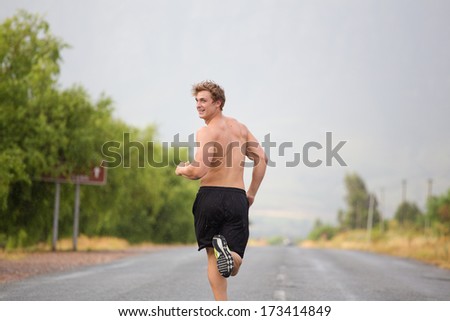Two male models running on a tarmac road, bare chested and wearing shorts and running shoes.