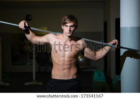 A Good looking male model flexing his muscles in a gym using weights, bare chest and wearing a short