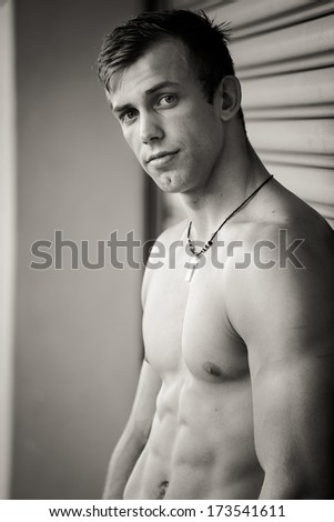 A close up portrait of a good looking male model standing against a roll up shutter door in an industrial area, bare chest and wearing a jean