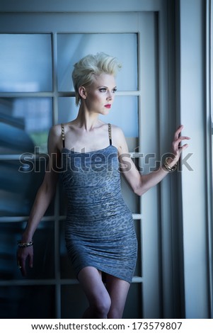 Sexy blond model standing against a wall at an open window