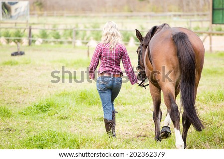 Sexy blond Farm Girl leading a horse in a paddock on a farm in South Africa