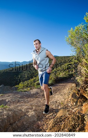 Male fitness model running allong a trail in the field on a bright sunny day with blue skies