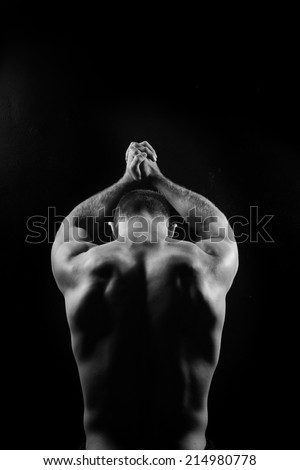 Male fitness model showing muscles in studio with a black background