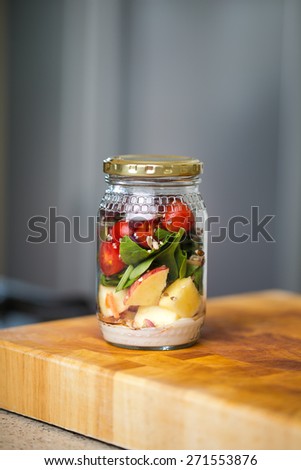Healthy fresh salad in a jar, ingredients include, Apple, Salad leaves, nuts, cherry tomatoes, mayonnaise and balsamic vinegar and olives.