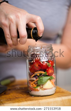 Healthy fresh salad in a jar, ingredients include, Apple, Salad leaves, nuts, cherry tomatoes, mayonnaise and balsamic vinegar and olives.
