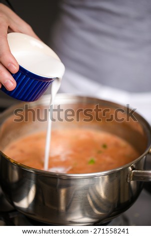 Close up image of a chef adding ingredients to a pot on a gas stove for a delicious thai soup. Ingredients include, chopped baby leaks, tomato relish, spices, coconut milk.