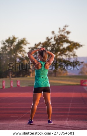 Female sprinter / athlete stands on a tartan race track stretching before a race.
