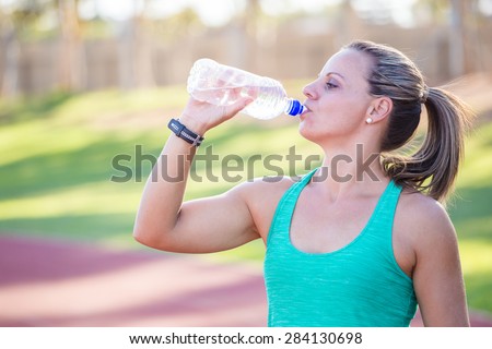Fit Female athlete drinking water from her water bottle on a tartan athletics track just before she starts training.