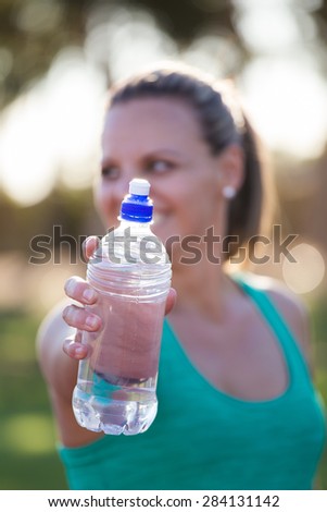 Fit female athlete holding out her water bottle towards the viewer just before she starts to train on a tartan athletics track