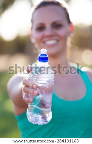 Fit female athlete holding out her water bottle towards the viewer just before she starts to train on a tartan athletics track