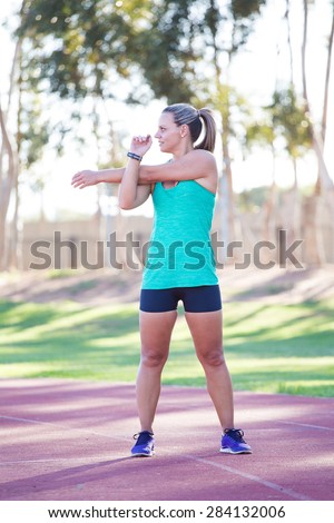 Fit and happy female athlete doing stretches before she starts training on a tartan athletics track.