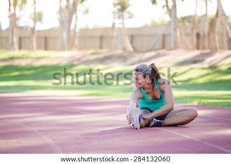 Fit and happy female athlete doing stretches before she starts training on a tartan athletics track.