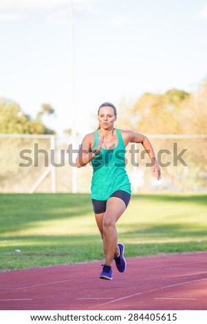 Fit female athlete spring on a tartan athletics track in the late afternoon.