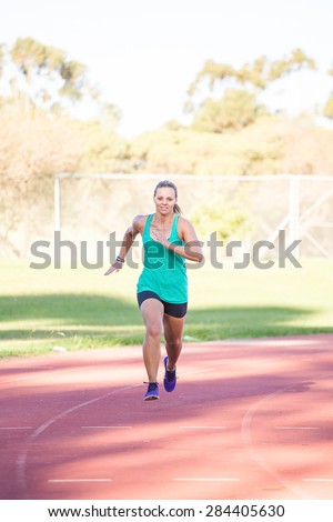 Fit female athlete spring on a tartan athletics track in the late afternoon.