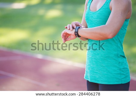 Fit female athlete looking at her watch with a heart rate monitor built in to track her progress of her exercise on a tartan athletics track.