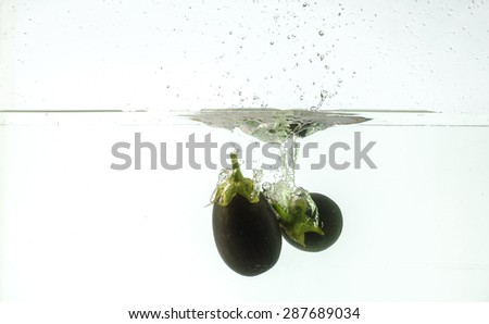 Close up image of an eggplant / aubergine being dropped into water on a white back ground