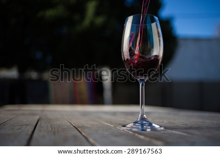 Close up wide angle   shot of a glass of red whine on a rustic table outside with natural light