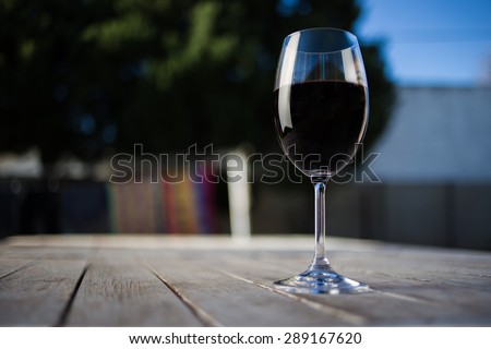 Close up wide angle shot of a glass of red whine on a rustic table outside with natural light