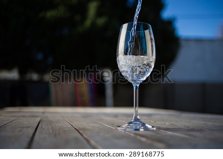 water being poured into a wine glass on a rustic table outside with natural light.