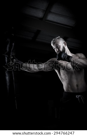 Male Athlete boxer punching a punching bag with dramatic edgy lighting in a dark studio