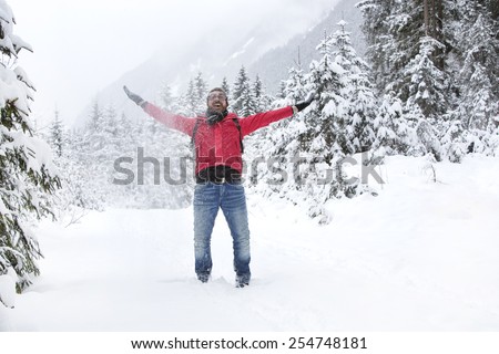 Happy young man with a red jacket and snow glasses throws up snow