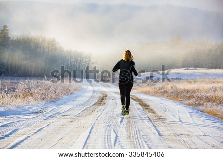 A female trail runs in the fog and snow of winter.