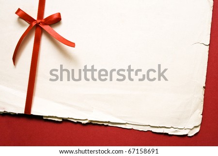 Red gift bow with ribbons and blank old paper on red paper