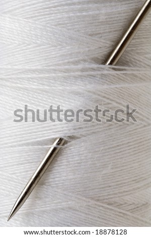closeup of a needle stuck in a spool of white thread