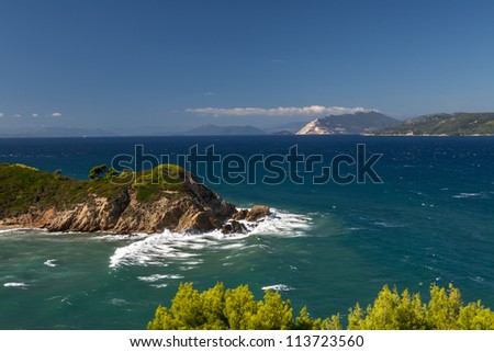 Rocky cape is washed by sea waves in front of distant mountains