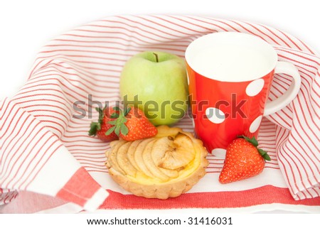 Apple, strawberries, apple cake and a cup of milk on a striped cloth