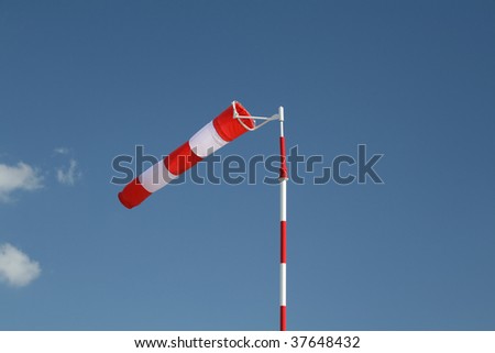 Flapping red and white striped windsock on a pole on the clear blue sky