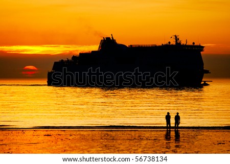 Two people looking on the ferry vessel in the sunsea on a seashore (silhouette)