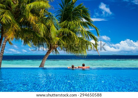 young couple relaxing in infinity pool under coco palms in front of tropical  landscape
