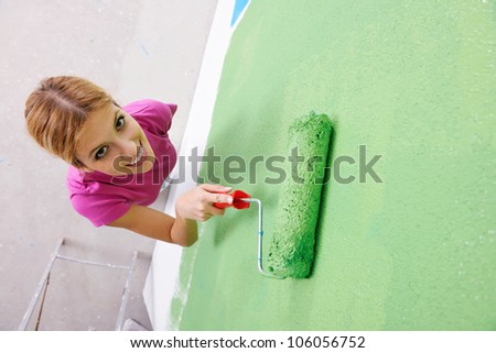 happy smiling woman painting interior white  wall in blue and green color of new house