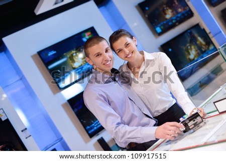 Young couple in consumer electronics store looking at latest laptop, television and photo camera to buy