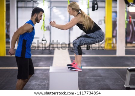 young athletic woman training with personal trainer  jumping on fit box at cross fitness gym