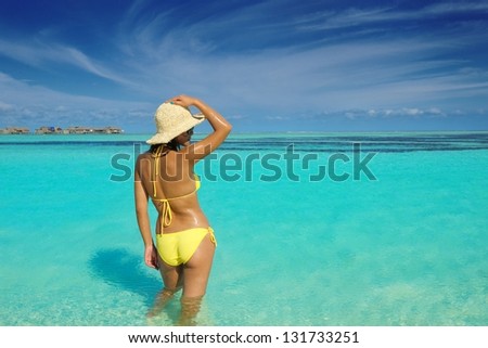 happy young beautiful asian woman relax on sand at tropical beach with cristal clear sea in background